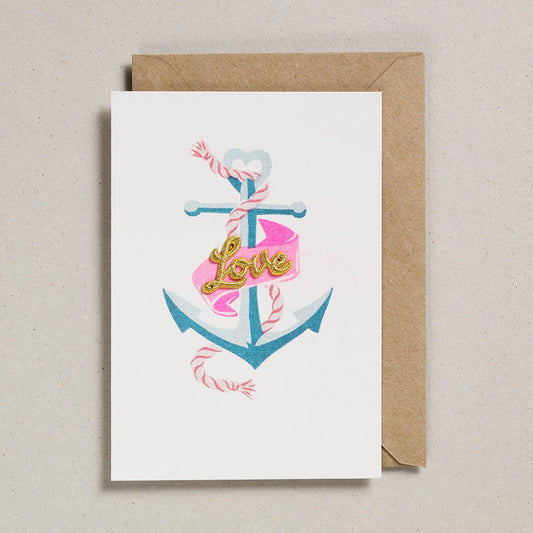 retro vintage style illustrated anchor in pale and baby blue tones with a pink and white rope and pink ribbon wrapped around it with a gold thread embroidered Love text attached to the ribbon mounted on a white card base with a kraft card envelope and sealed in a biodegradable cellophane bag